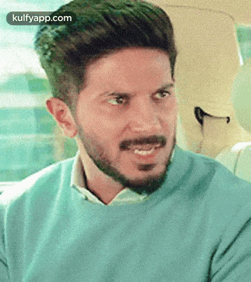 a man with a beard is wearing a blue sweater and a white shirt .