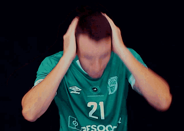 a man wearing a green jersey with the number 21 covering his ears
