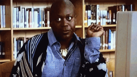a bald man sitting in front of a computer monitor in a library