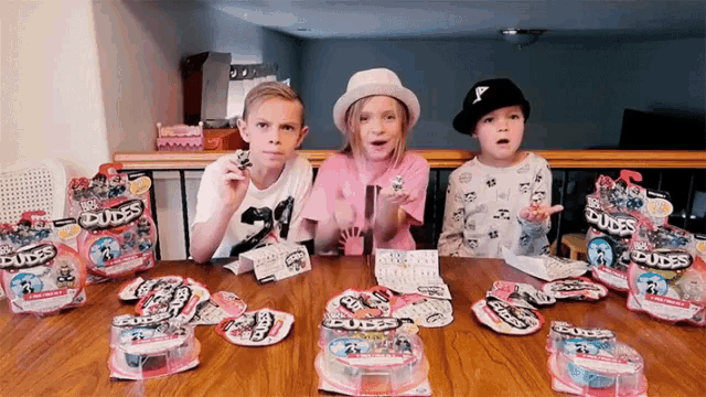 three children sit at a table with packages of dudes