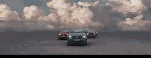 a group of cars are driving down a dirt road .