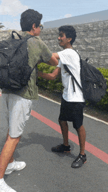 a man wearing a white shirt that says ' california ' on it shakes hands with another man wearing a black backpack