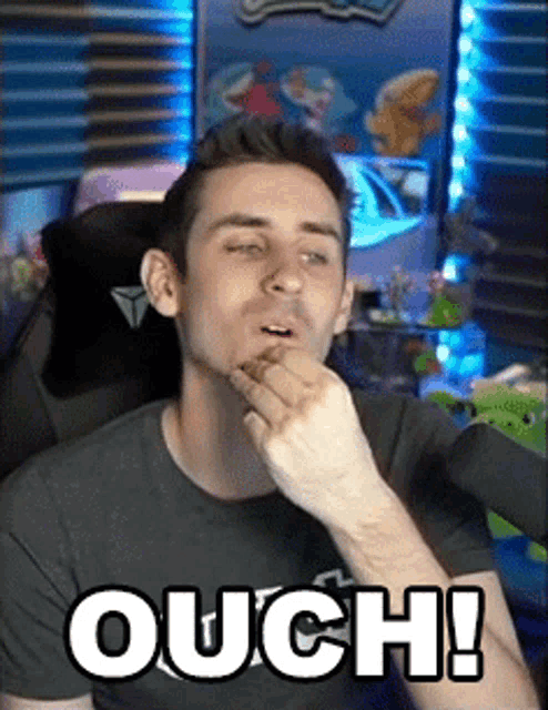 a man is sitting in a chair with his hand to his mouth and the words ouch written on the screen .