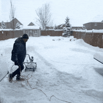 a man is pushing a snow blower down a snowy path