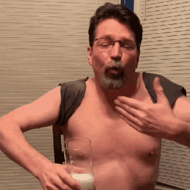 a shirtless man holds a glass of milk in his hand