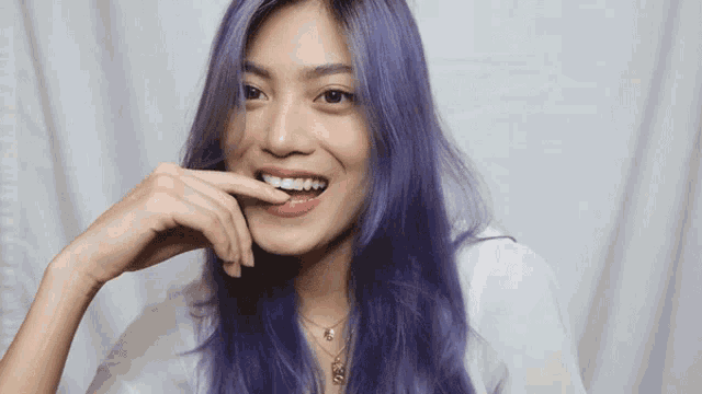 a woman with purple hair is smiling with her hand on her mouth