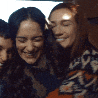 three women are hugging and smiling and one of them is wearing a sweater that says lvb