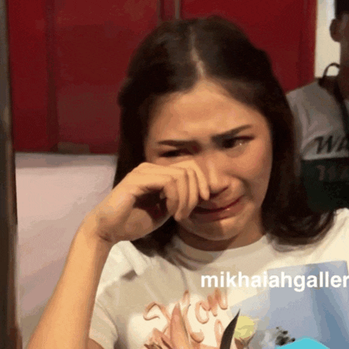a woman wipes her face with her hand and the words mikhaelgallian are visible in the corner