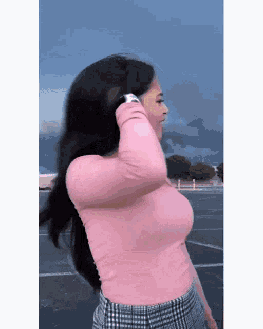 a woman wearing a pink top and plaid skirt stands in a parking lot