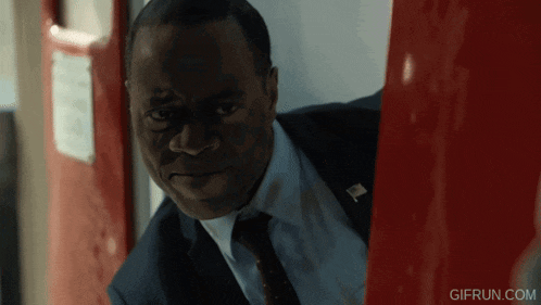 a man in a suit and tie is standing in front of a red door with gifrun.com on the bottom