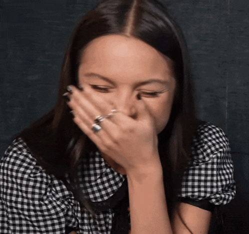 a woman in a plaid shirt is covering her face with her hand .