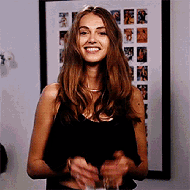a woman in a black tank top is smiling and holding a glass of wine