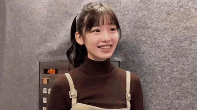 a young woman is smiling in front of an elevator with the number 450 on the screen .