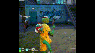 a person in a clown costume is holding a gun in front of a graffiti wall .