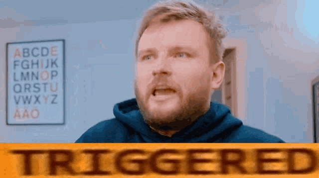 a man in a blue hoodie is standing in front of a sign that says triggered