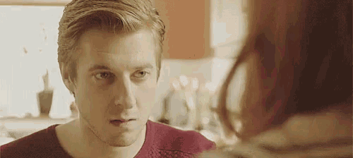 a man in a red sweater is looking at a woman in a mirror .