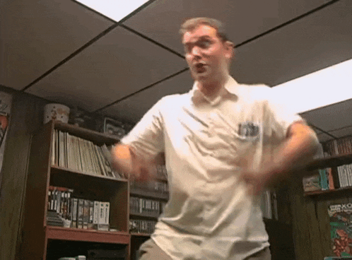 a man in a white shirt is dancing in front of a bookshelf filled with books .