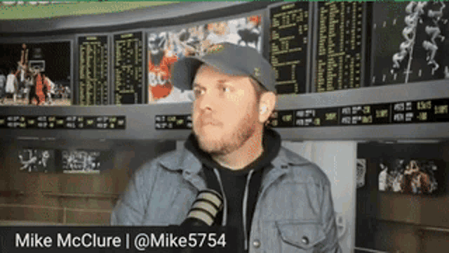 a man wearing a hat and a jacket is standing in front of a screen that says mike mcclure