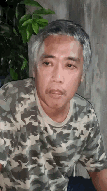 a man in a camo shirt looks at the camera