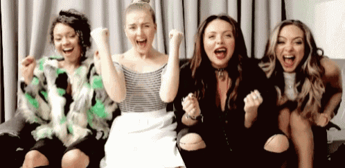 a group of four women are sitting on a couch with their arms in the air .