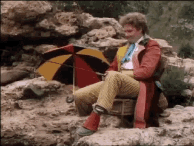 a man is sitting on a rock with an umbrella in his hand .