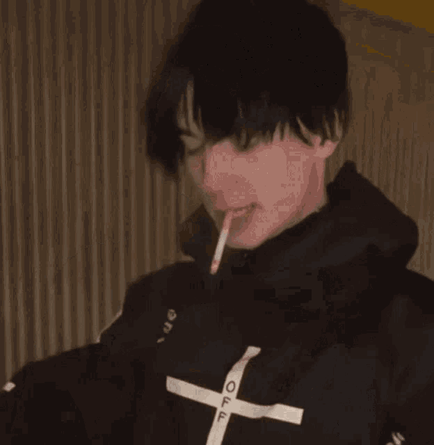 a young man is smoking a cigarette while looking at a laptop .