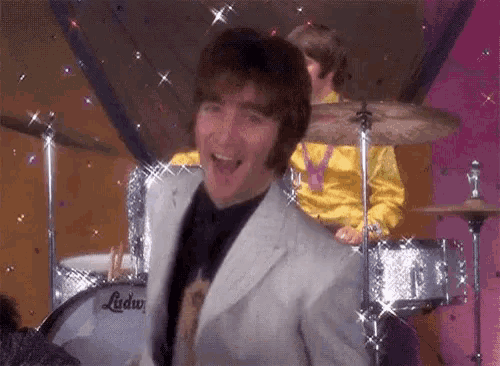 a man in a suit is standing in front of a drum set and smiling .