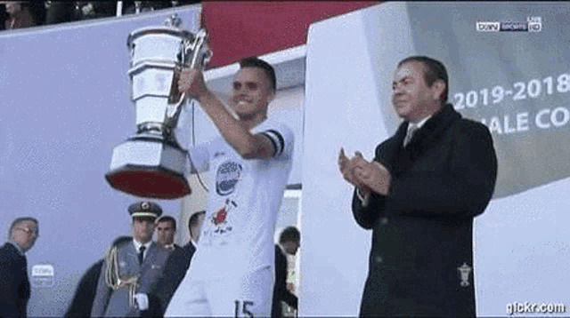 a soccer player is holding a trophy in his hand while a man applauds .