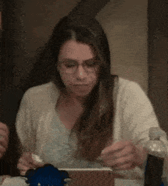 a woman wearing glasses is sitting at a table looking at a tablet