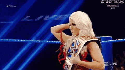 a woman is standing in a wrestling ring holding a wrestling championship belt .
