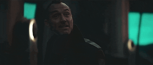 a man in a black jacket is standing in a dark room looking at something .