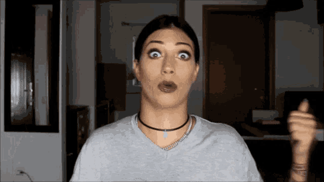 a woman wearing a choker necklace and a grey shirt is making a funny face