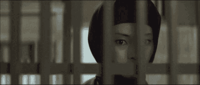 a woman is behind bars in a jail cell looking through the bars .