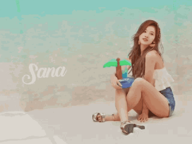 a woman is sitting on the beach holding an inflatable palm tree and the name sana is on the wall behind her
