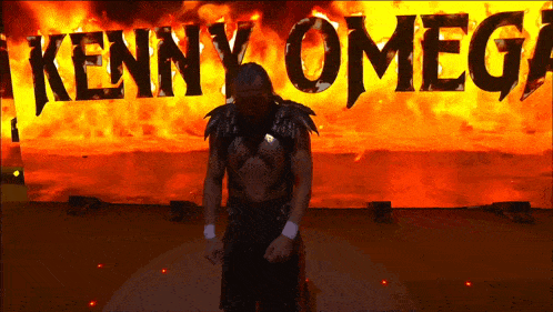 a wrestler named kenny omega is standing in front of a fire background