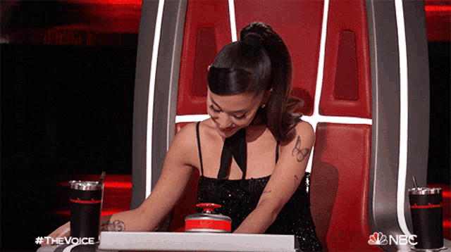a woman in a black dress sits in a chair with a nbc logo on the back