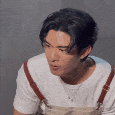 a young man wearing a white shirt and suspenders looks at the camera