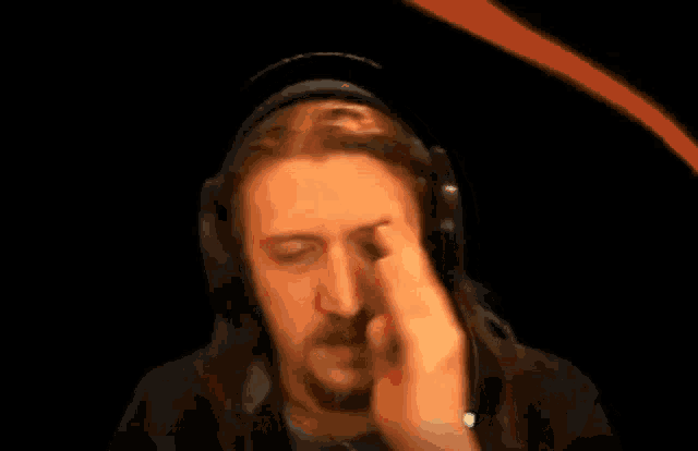 a man with long hair and a beard is wearing headphones and rubbing his eyes