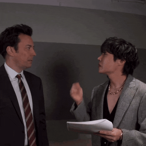 a man in a suit and tie blows a kiss to another man in a plaid jacket