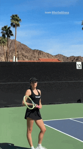 a woman holding a tennis racquet on a tennis court with the number 12 behind her