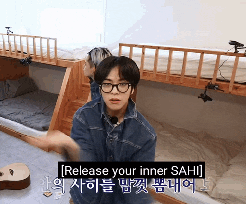 a man wearing glasses and a denim jacket is standing in front of a bunk bed and says release your inner sahi