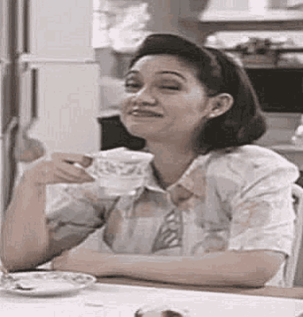a woman is sitting at a table holding a cup of coffee and smiling .