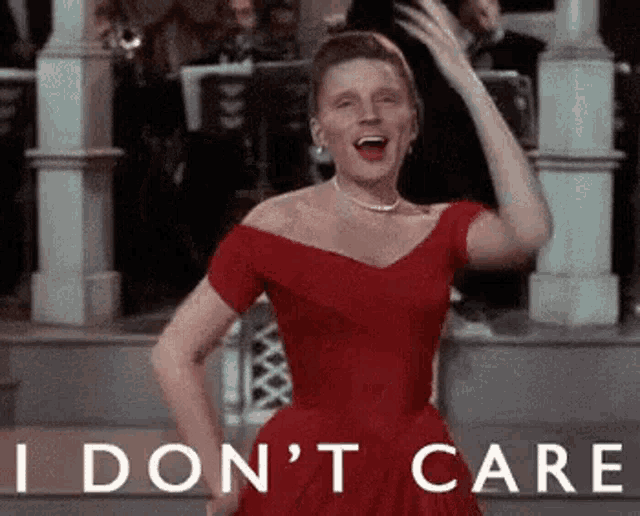 a woman in a red dress is dancing in front of an orchestra and saying `` i do n't care '' .