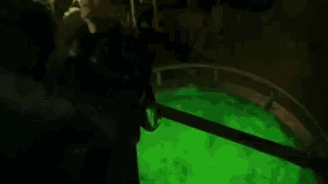 a man is hanging from a pipe in a dark room with a green light .