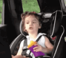 a little girl is sitting in a car seat holding a purple bag of chips .