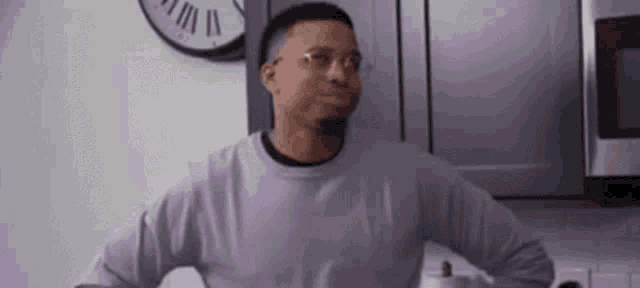 a man in a purple sweater and glasses is standing in a kitchen with his arms outstretched .