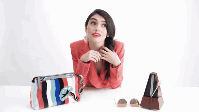 a woman in a red jacket sits at a table with a striped purse and a metronome
