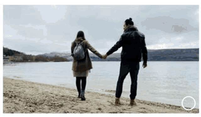 a man and a woman are holding hands while walking along the beach .