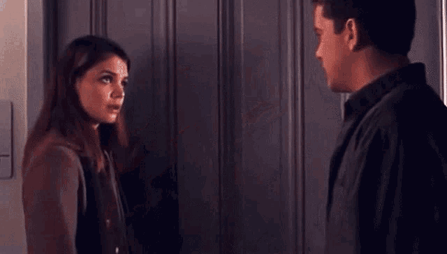 a man and a woman are standing next to each other in front of a door and looking at each other .