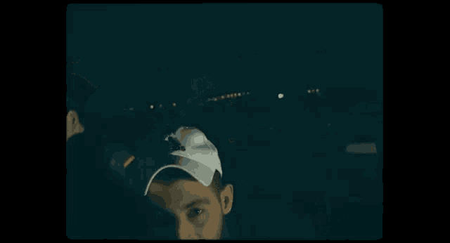 a man wearing a baseball cap is smiling and looking at the camera in a dark room .